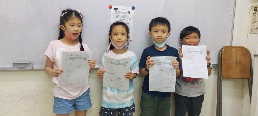 Four children stand inside against a wall, holding up their Galaxy Scouts activity drawings. They are smiling.